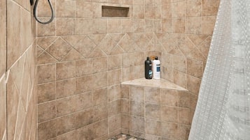 A shower area with a handheld showerhead, a wall-mounted faucet, and a tiled floor with a geometric pattern.