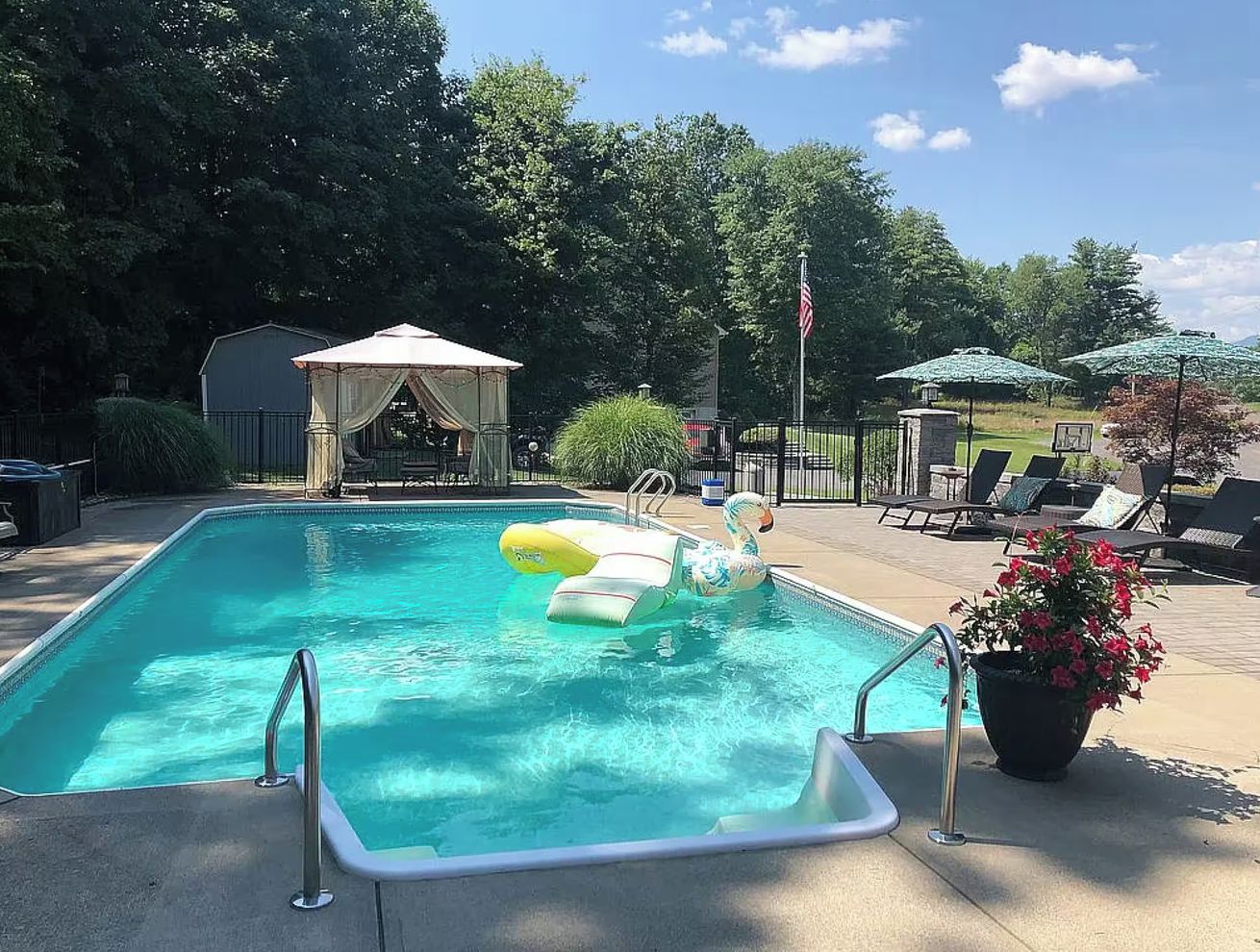 A rectangular swimming pool with a slide, surrounded by lounge chairs and a gazebo.
