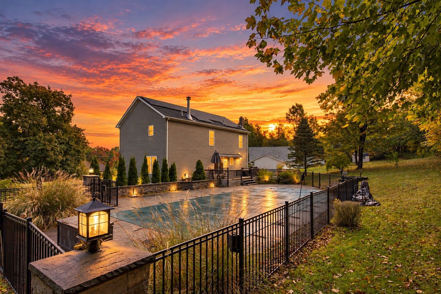 A house with a swimming pool, surrounded by a fence, and a sunset in the background.