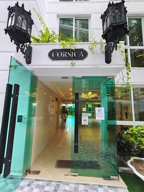 A hotel entrance with a glass door, a sign above reading 'CORSICA', and two black lantern-style lights. - City Olympus Garden Condominium - 1 luxury bedroom - 5 swimming pools in Pattaya (Muang Pattaya)