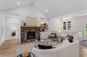 A living room with a stone fireplace, a sofa, a coffee table, and a lamp. - NEW Saugatuck sleeps 12_Pool_Hot Tub_Game Room (Hamilton)