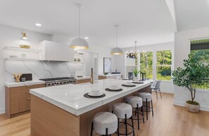 A modern kitchen with a large island, pendant lighting, and a view of the outdoors. - NEW Saugatuck sleeps 12_Pool_Hot Tub_Game Room (Hamilton)