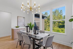 A dining area with a table, chairs, a chandelier, and large windows with a view of trees. - NEW Saugatuck sleeps 12_Pool_Hot Tub_Game Room (Hamilton)
