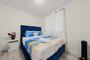 Une chambre à coucher avec un lit, une table de chevet, une plante en pot et un radiateur portatif.