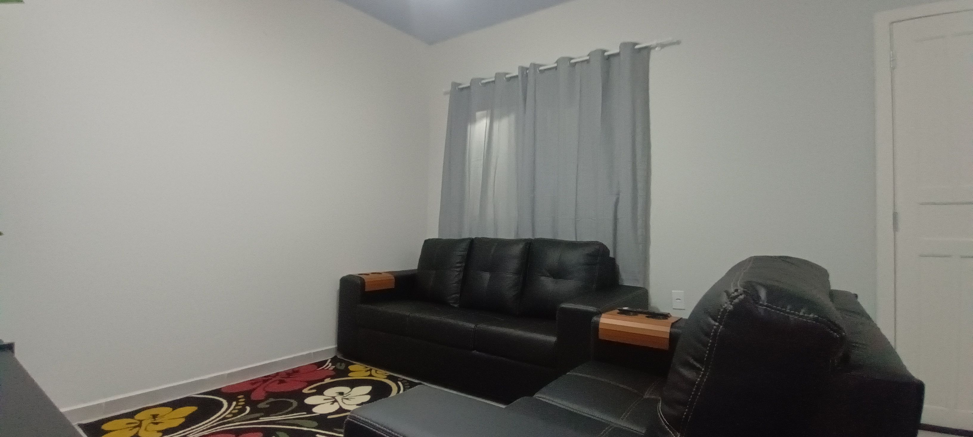 Ein kleiner, kompakter Wohnraum mit einem schwarzen Ledersofa, einem kleinen Tisch und einem gemusterten Teppich.
