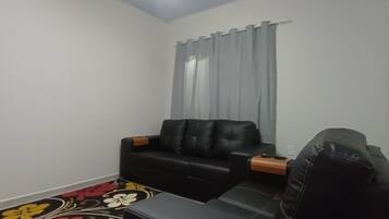 Ein kleiner, kompakter Wohnraum mit einem schwarzen Ledersofa, einem kleinen Tisch und einem gemusterten Teppich.