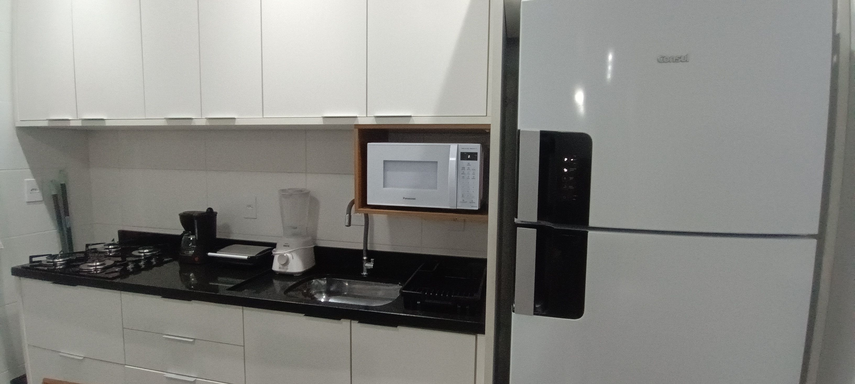 Eine Küche mit weißen Schränken, einer schwarzen Arbeitsplatte, einer eingebauten Mikrowelle und einem Kühlschrank.