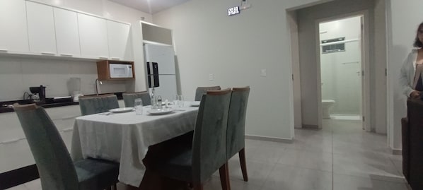 A dining area with a table set for four, chairs, a microwave, and a refrigerator.