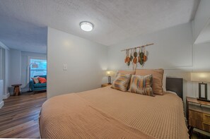 Ein Schlafzimmer mit einem großen Bett, zwei Nachttischlampen, einer Wanddekoration aus Makramee und einem Nachttisch aus Holz.