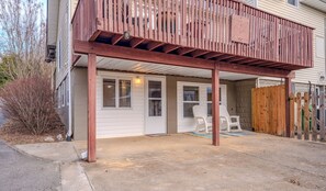Ein überdachter Patio-Bereich mit Holzboden, einer weißen Tür und einer kleinen Sitzecke mit Plastikstühlen.