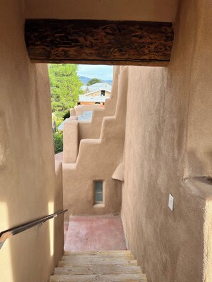 A corridor with a wooden staircase leading to a window, surrounded by textured walls. - Unique 1-bedroom Adobe casa apartment with beautiful deck in Albuquerque, (Albuquerque)