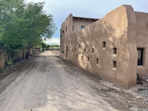 Ein Feldweg führt zu einem Gebäude mit Stuckfassade und zahlreichen Fenstern.