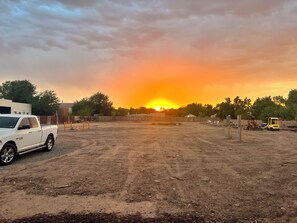Ein unbefestigter Parkplatz mit einem weißen Pickup-Truck auf der linken Seite, einem gelben Bagger auf der rechten Seite und einem Sonnenuntergang im Hintergrund.