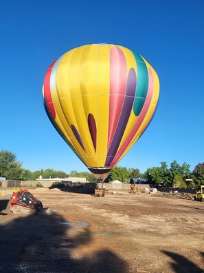 Eine Heißluftballon ist auf einem unbefestigten Boden geparkt, im Hintergrund sind Baumaschinen zu sehen.
