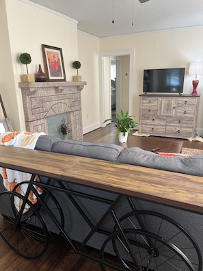 A living room with a sofa, a fireplace, a television, and a wheelchair-accessible table. - Cozy 2-bedroom cottage in a country setting in Ruffin NC (Ruffin)