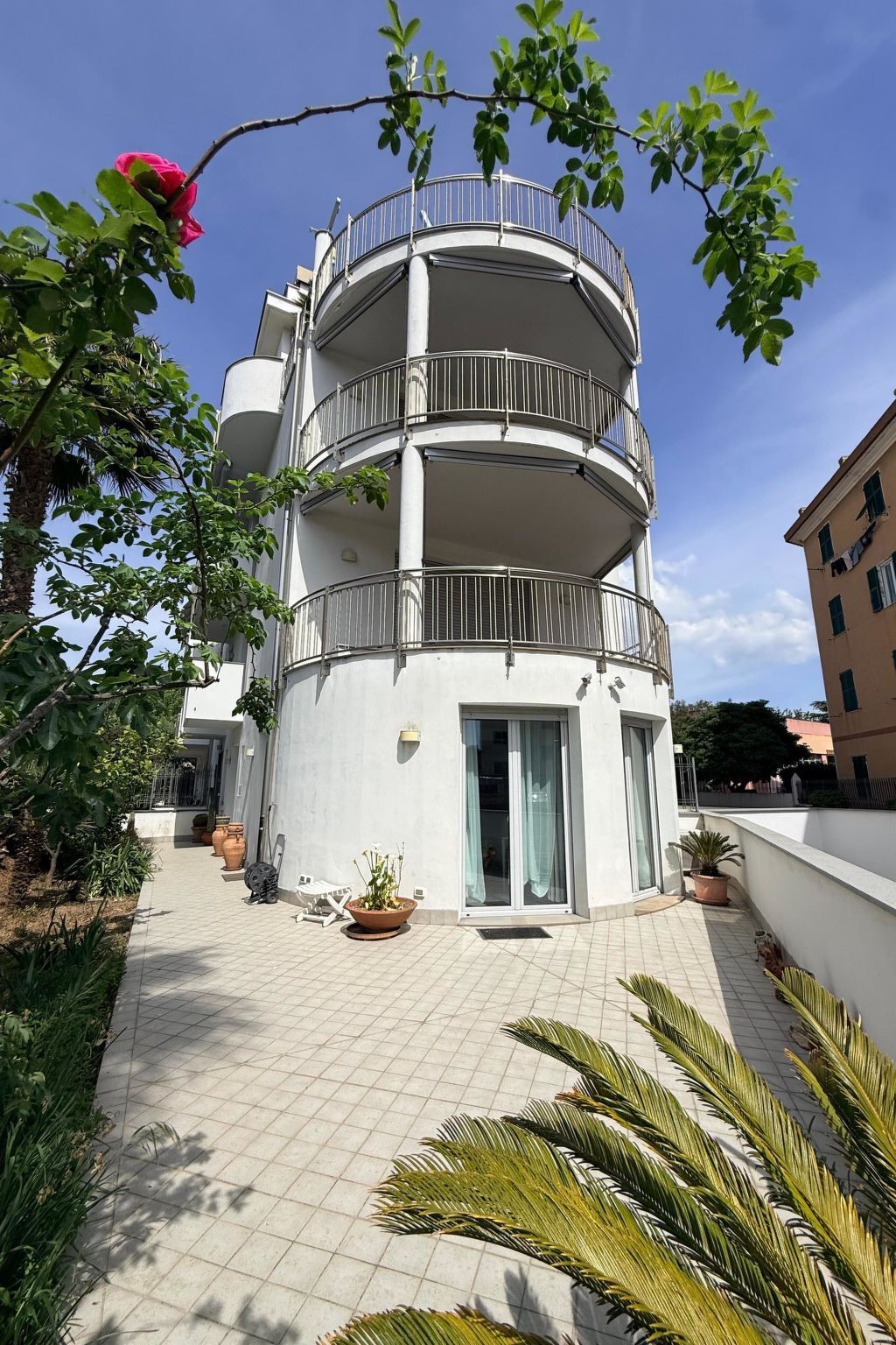 A multi-story residential building with balconies, a tiled patio, and potted plants.