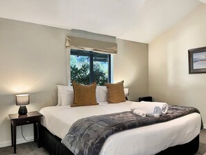 Ein Hotelzimmer mit einem Bett, einem Fenster mit Blick, einem Nachttisch mit Lampe und einem gerahmten Bild an der Wand.