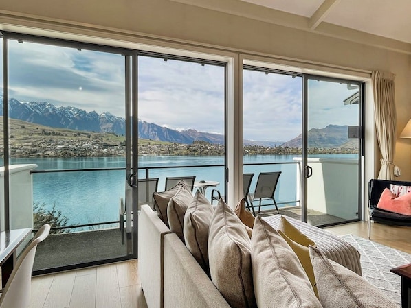 A balcony with a view of a lake and mountains, a sofa with cushions, and a table with chairs. - Alpine Lakefront Villa, 2 Bath, Queenstown (Queenstown)