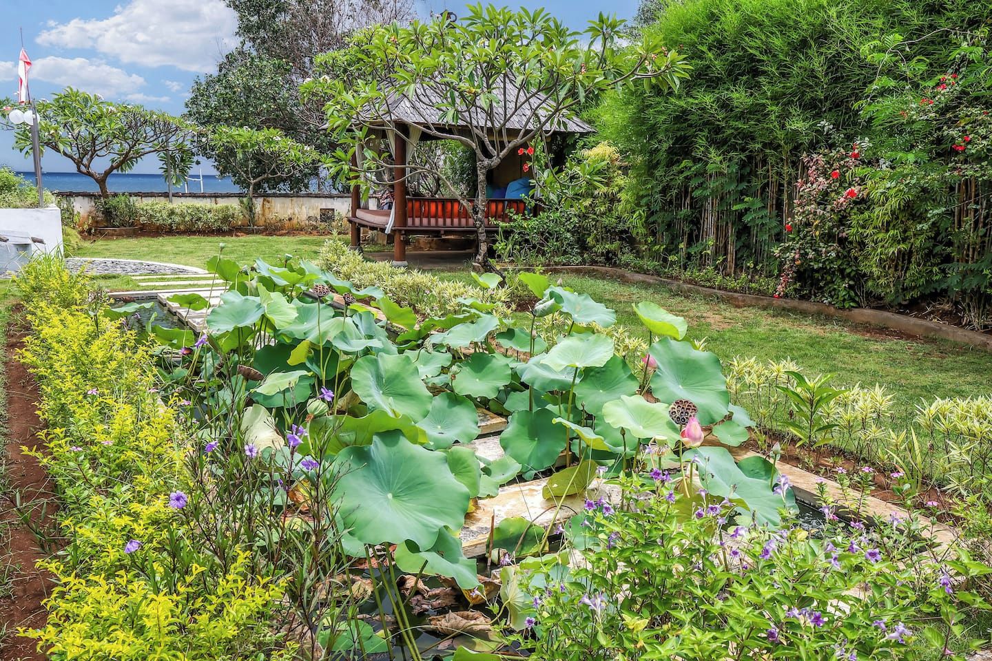 Um jardim com um coreto, plantas de lótus e diversas outras folhagens.
