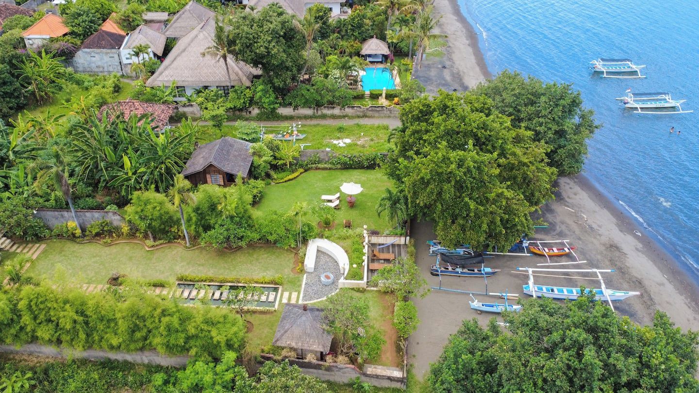 An aerial view of a coastal property with a swimming pool, boats, and lush greenery.