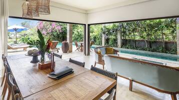 A dining area with a wooden table, chairs, and a view of a swimming pool and garden.