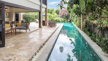 A swimming pool with a stone-lined edge, surrounded by lush greenery and a patio area with outdoor furniture.