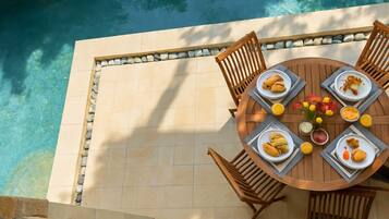 Zona pranzo a bordo piscina con tavolo rotondo, sedie e vista sulla piscina.