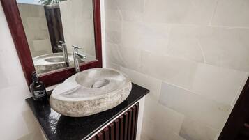 A bathroom with a stone sink, a mirror, and a black countertop.