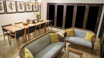 A dining area with a wooden table and chairs, a sofa with cushions, and a wall with framed artwork.