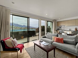 Ein modernes Wohnzimmer mit einer Couch, einem Couchtisch und Blick auf eine Berglandschaft durch große Glasfenster.