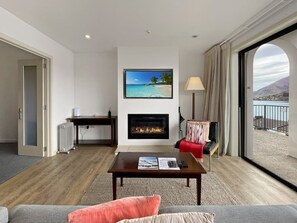 Sala de estar com lareira, televisão e vista para a praia através de uma grande janela.