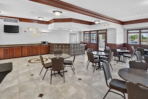 A spacious dining area with multiple tables and chairs, a kitchen area with a microwave, and a television mounted on the wall.