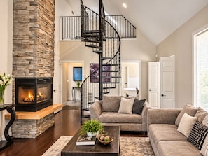 A living room with a stone fireplace, a black spiral staircase, and a large gray sofa.