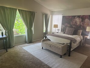 Une chambre à coucher comprenant un lit, une table de chevet, une lampe, une fenêtre avec des rideaux et un grand décor mural représentant des motifs floraux.