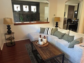 A living room with a sofa, two lamps, a coffee table with decorative items, a mirror, and a dining area in the background. - Elegant 4-bedroom 2,5 bath furnished & renovated house in beautiful Newbury Park (Thousand Oaks)