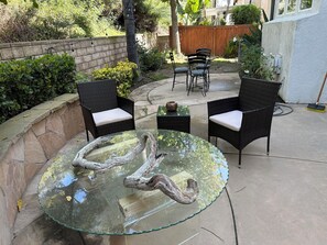 An outdoor patio with a glass table featuring a natural wood centerpiece, surrounded by wicker chairs with cushions. - Elegant 4-bedroom 2,5 bath furnished & renovated house in beautiful Newbury Park (Thousand Oaks)