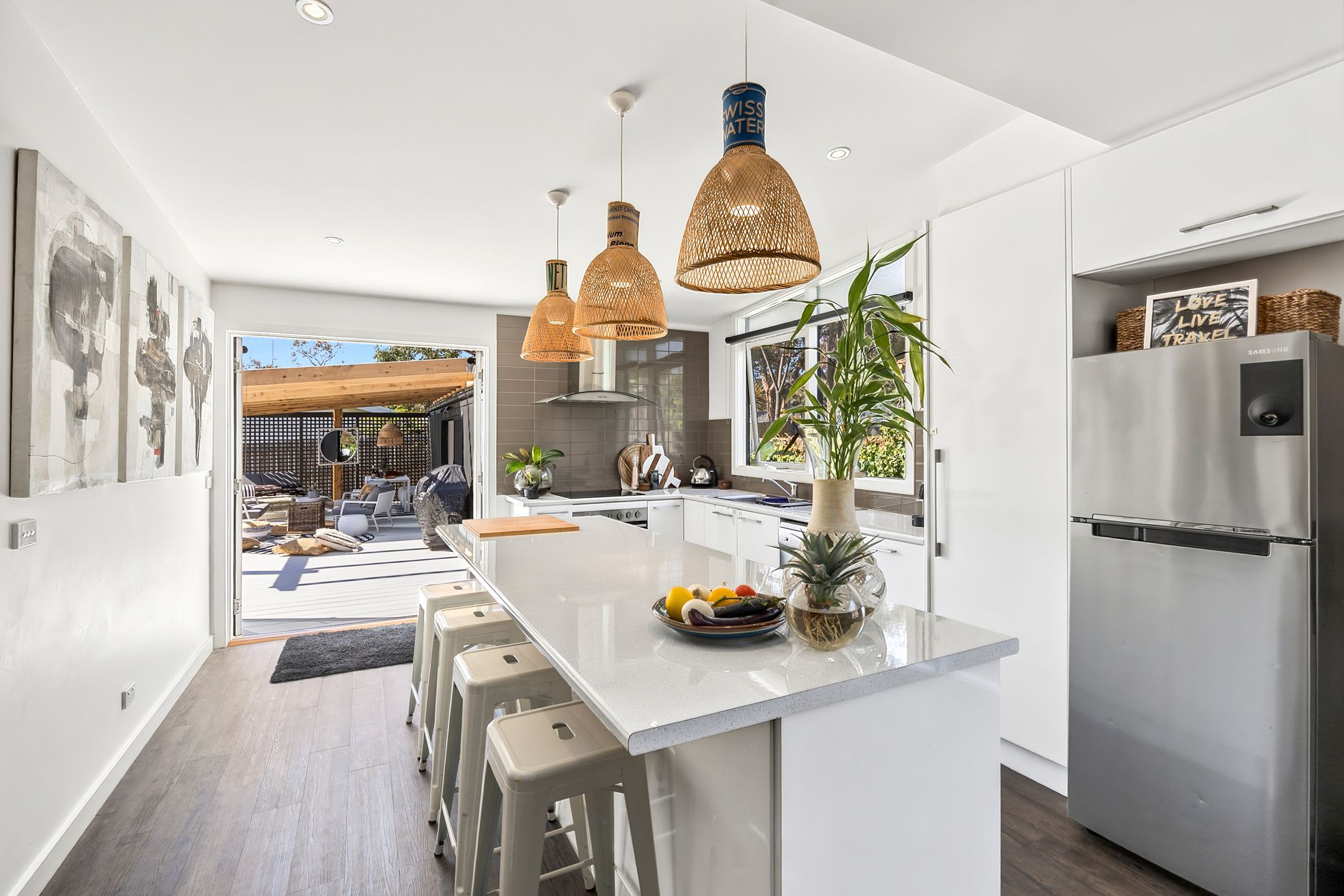 A modern kitchen with white cabinetry, a central island with stools, pendant lighting, and a refrigerator.