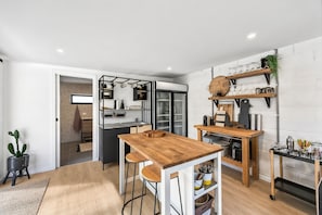 A modern kitchen with a wooden table, bar stools, and a built-in refrigerator. - Links & Leisure Retreat - Relaxed Coastal Stay (Anglesea)