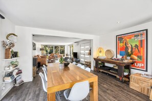 A modern living space with a wooden dining table, white chairs, a sofa, and a television. - Links & Leisure Retreat - Relaxed Coastal Stay (Anglesea)