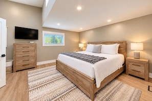 A bedroom with a wooden bed, bedside tables, a TV, and a window with blinds. - Pink Skies Landing | Steps to Powers Lake Beach (Genoa City)