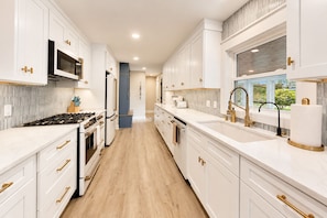 A modern kitchen with white cabinetry, stainless steel appliances, and a wooden floor. - Pink Skies Landing | Steps to Powers Lake Beach (Genoa City)