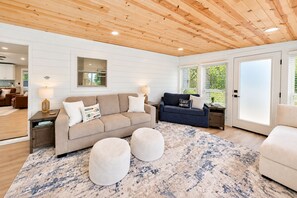 Ein modernes Wohnzimmer mit Holzboden, einem beigen Sofa, einem dunkelblauen Sofa und einem gemusterten Teppich.