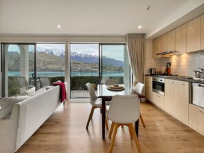 A modern kitchen with a view of a lake and mountains, a dining area with a table and chairs, and a sofa with a view. - Cosy Alpine Lakeview Suite for Couples (Queenstown)