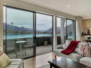 Sala de estar moderna com porta de vidro deslizante que dá para uma varanda com vista panorâmica de um lago e montanhas.