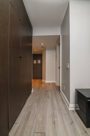 A hallway with wooden flooring, a dark wardrobe, and a door leading to another room. - Central Spacious Yorkville Suite (Toronto)
