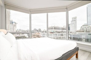 A bedroom with a large bed, a view of a cityscape through floor-to-ceiling windows, and a balcony with a railing. - Central Spacious Yorkville Suite (Toronto)