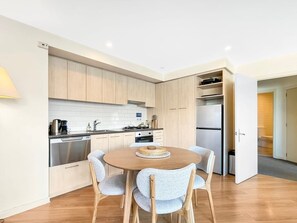 Eine moderne Küche mit hellen Holzschränken, einem Edelstahlkühlschrank und einem Esstisch mit vier Stühlen.