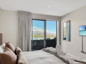 A hotel room with a bed, a view of a mountainous landscape, and a television on the wall. - Tranquil 1 Bed Corner Suite, Lake & Mountain Views (Queenstown)