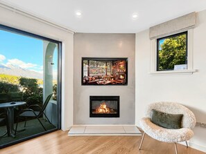 Ein modernes Wohnzimmer mit Kamin, einem Essbereich mit Tisch und Stühlen sowie einem großen Fenster mit Blick ins Freie.