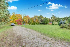 A grassy area with a dirt path leading to a parked car, surrounded by trees with autumn foliage. - Lakefront Adventure Cottage | Sleeps 10 | Kayaks, Dock & Hot Tub (Kawartha Lakes)